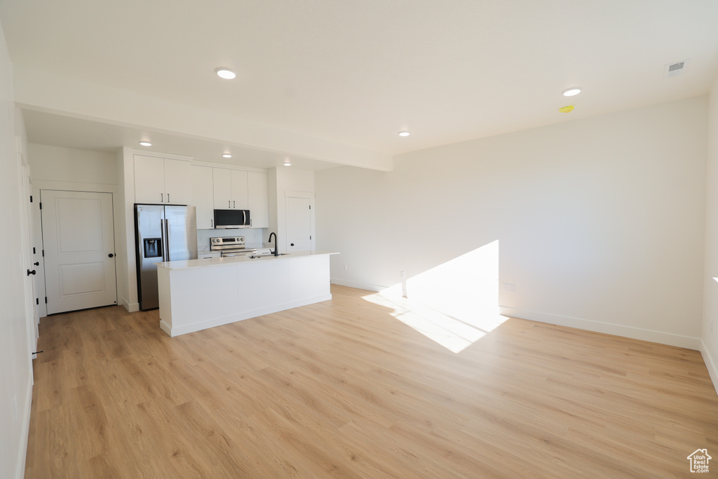 Kitchen with light wood-style flooring, a sink, a center island with sink, and appliances with stainless steel finishes