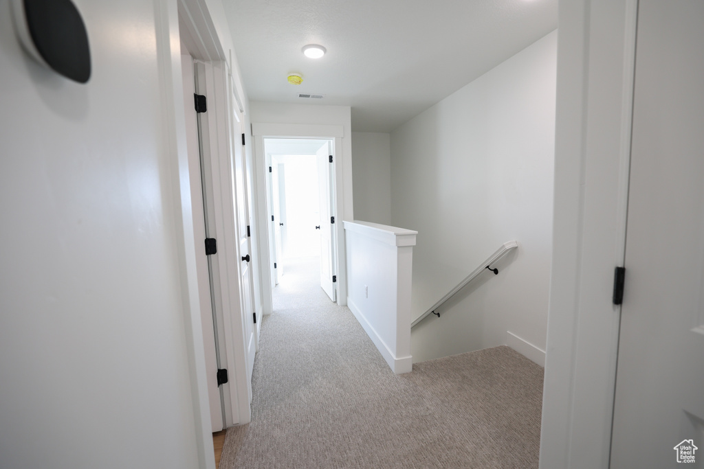 Corridor with light carpet, visible vents, and an upstairs landing