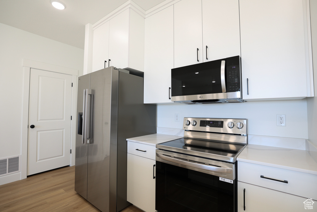 Kitchen with white cabinetry, light countertops, stainless steel appliances, and visible vents