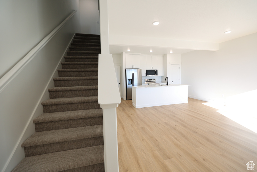 Stairs with recessed lighting, beamed ceiling, and wood finished floors
