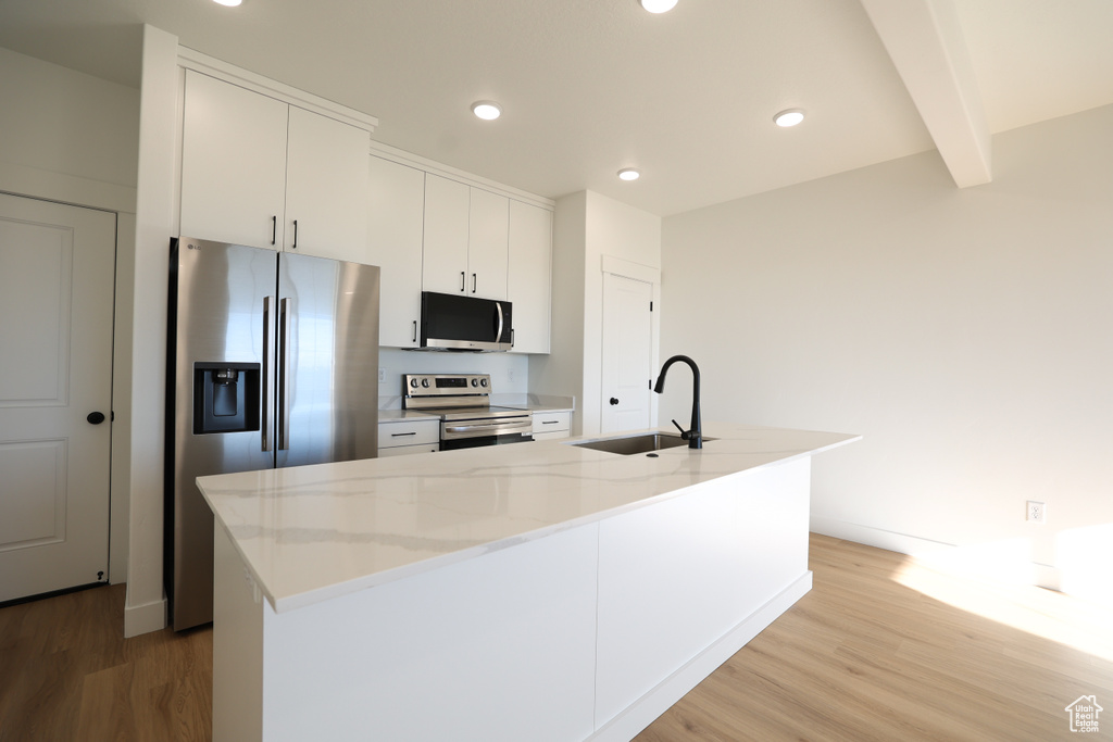 Kitchen with light wood finished floors, a sink, white cabinets, and appliances with stainless steel finishes