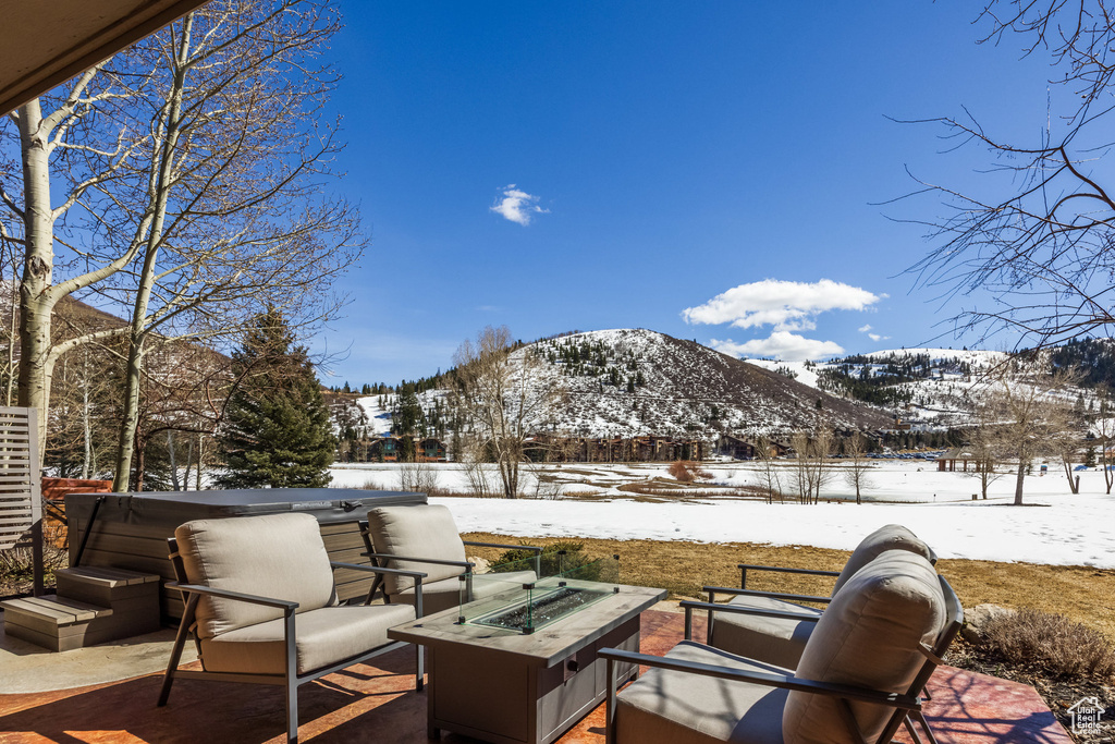Snow covered patio with a fire pit, a hot tub, a mountain view, and fence