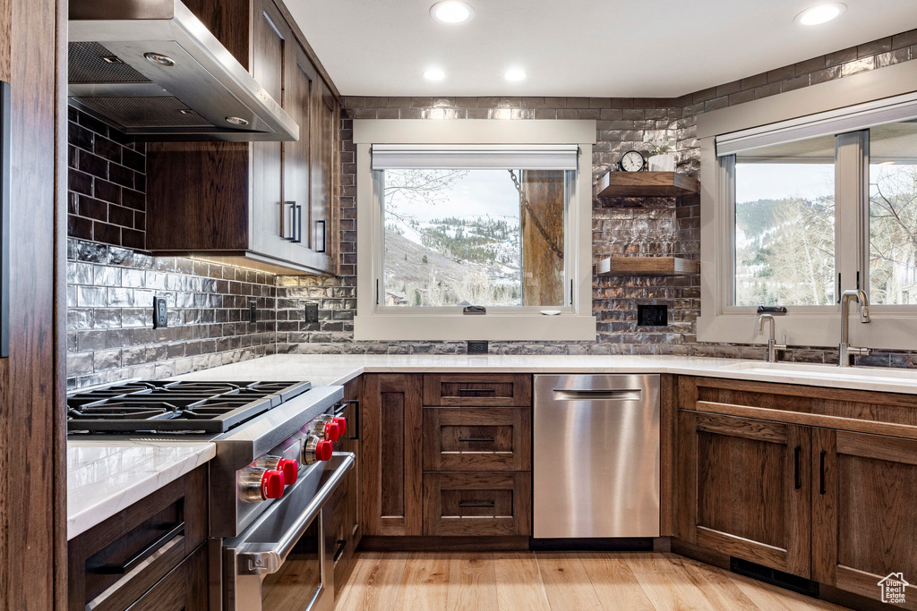 Kitchen with light countertops, appliances with stainless steel finishes, a sink, exhaust hood, and backsplash