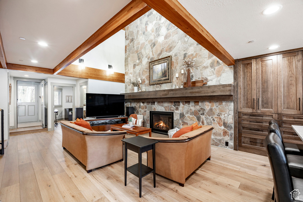 Living area with a stone fireplace, light wood finished floors, and beam ceiling
