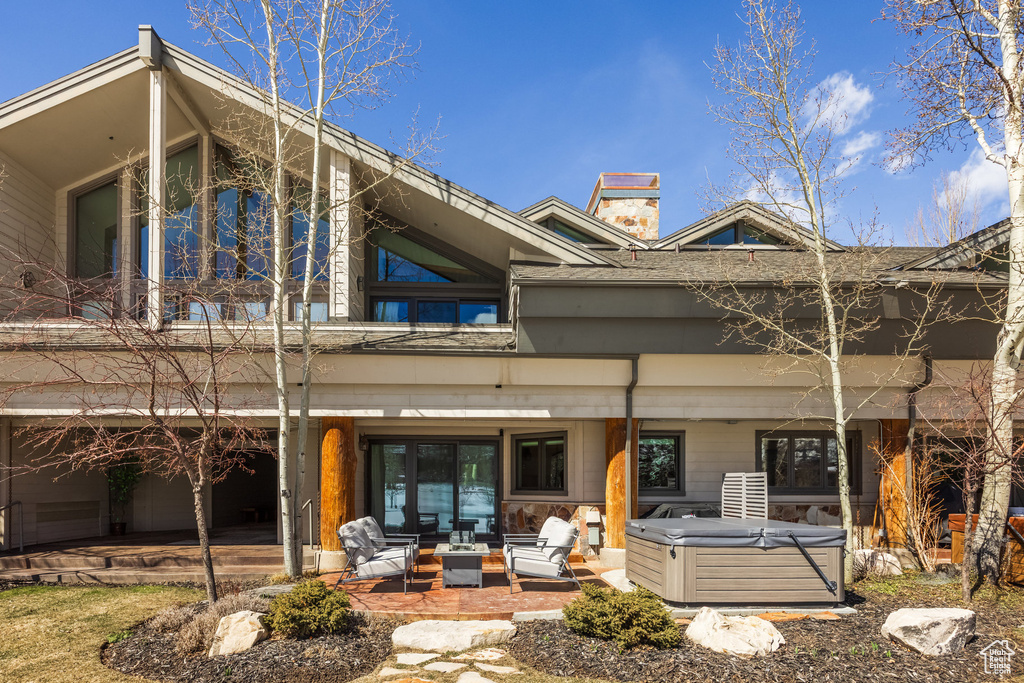 Rear view of property with a chimney, a shingled roof, a hot tub, and a patio area