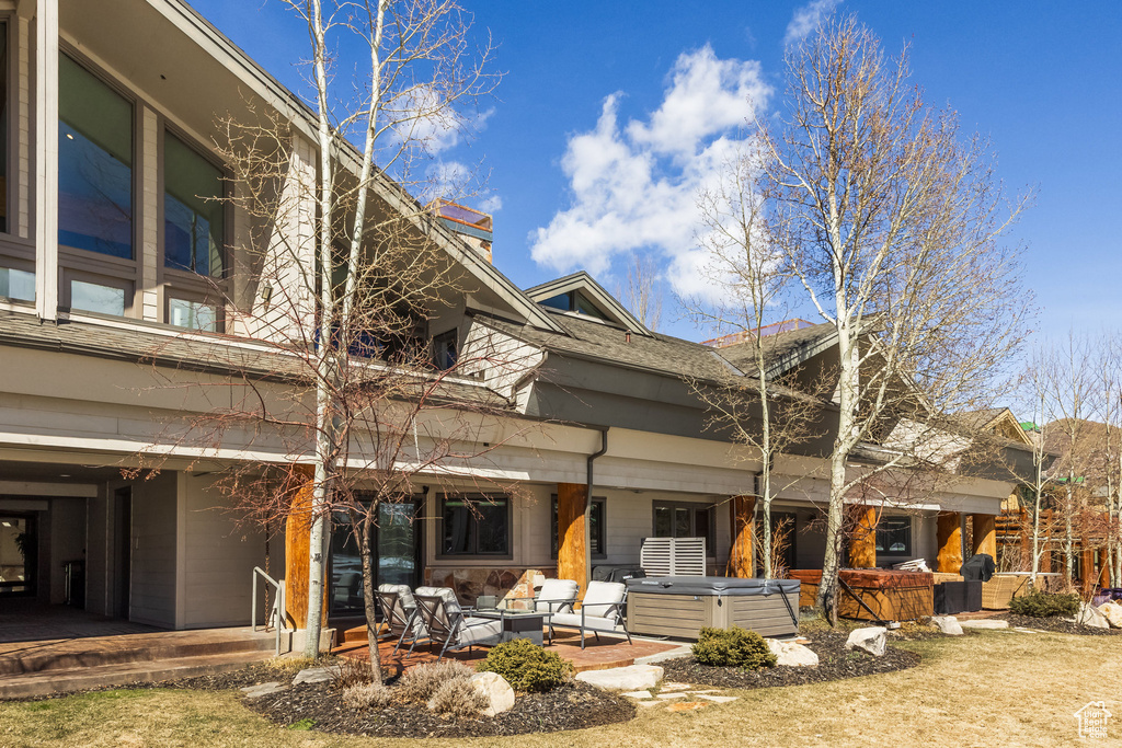 Rear view of house featuring outdoor lounge area, roof with shingles, a hot tub, and a patio area