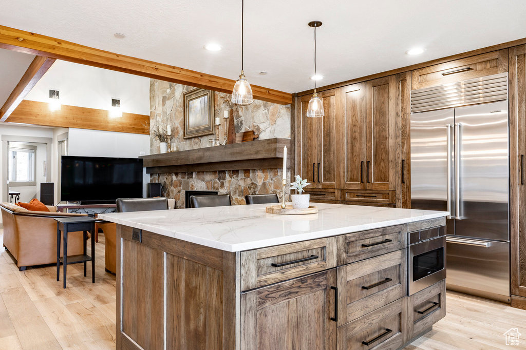 Kitchen with built in appliances, light stone counters, and light wood-style flooring