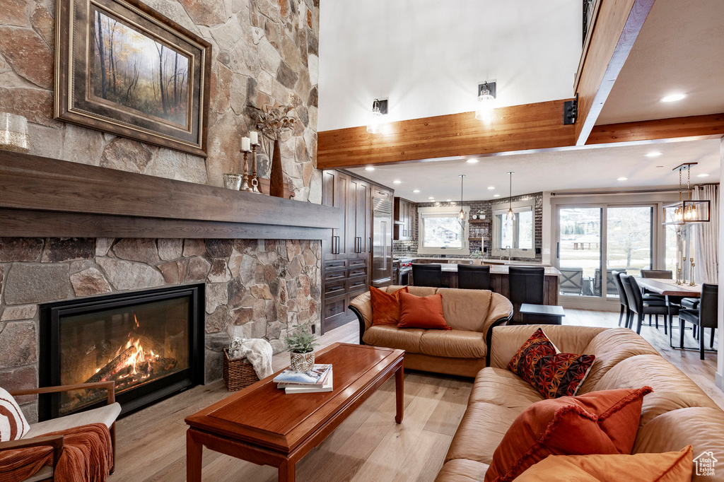 Living room with a fireplace, a high ceiling, beamed ceiling, and light wood finished floors