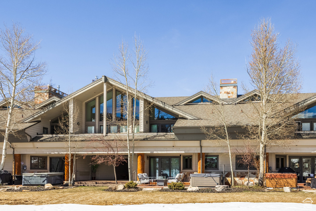 Rear view of house featuring a chimney, roof with shingles, a patio area, and a hot tub