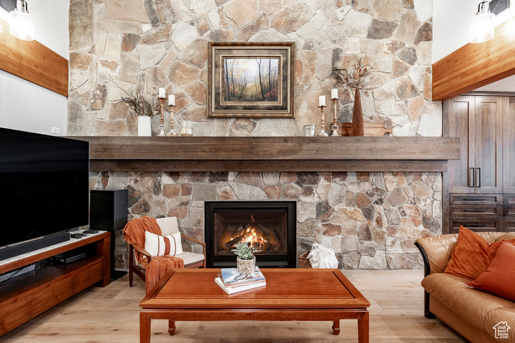 Living area featuring beamed ceiling, light wood-type flooring, and a stone fireplace