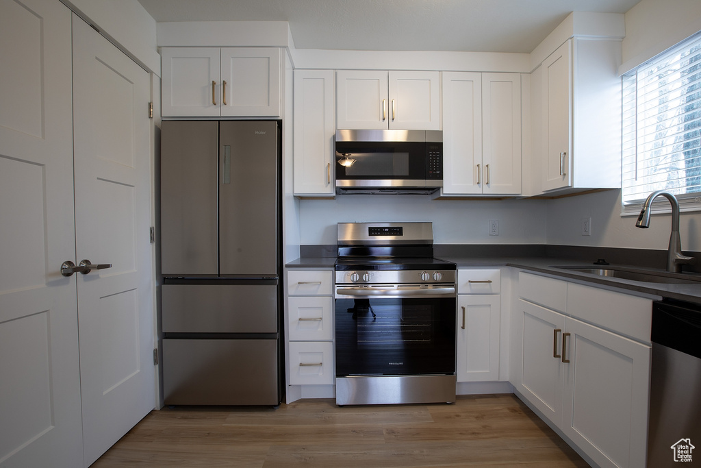 Kitchen with stainless steel appliances, a sink, dark countertops, and white cabinetry