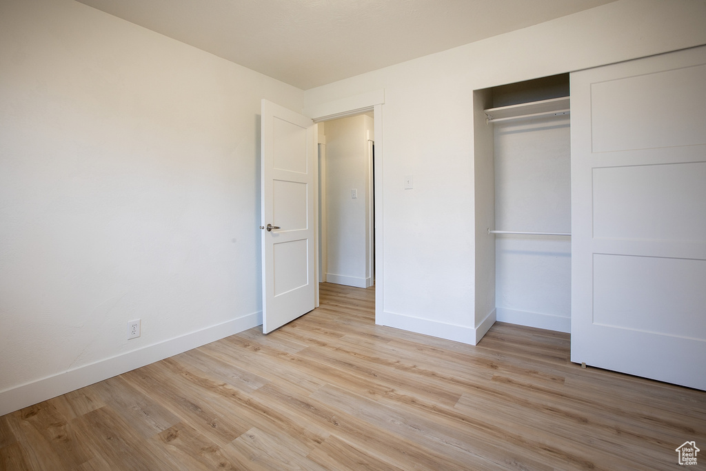 Unfurnished bedroom featuring light wood-type flooring, baseboards, and a closet