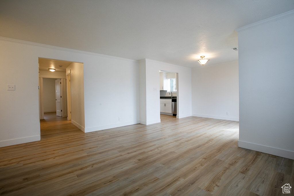 Empty room with light wood-type flooring, baseboards, and ornamental molding