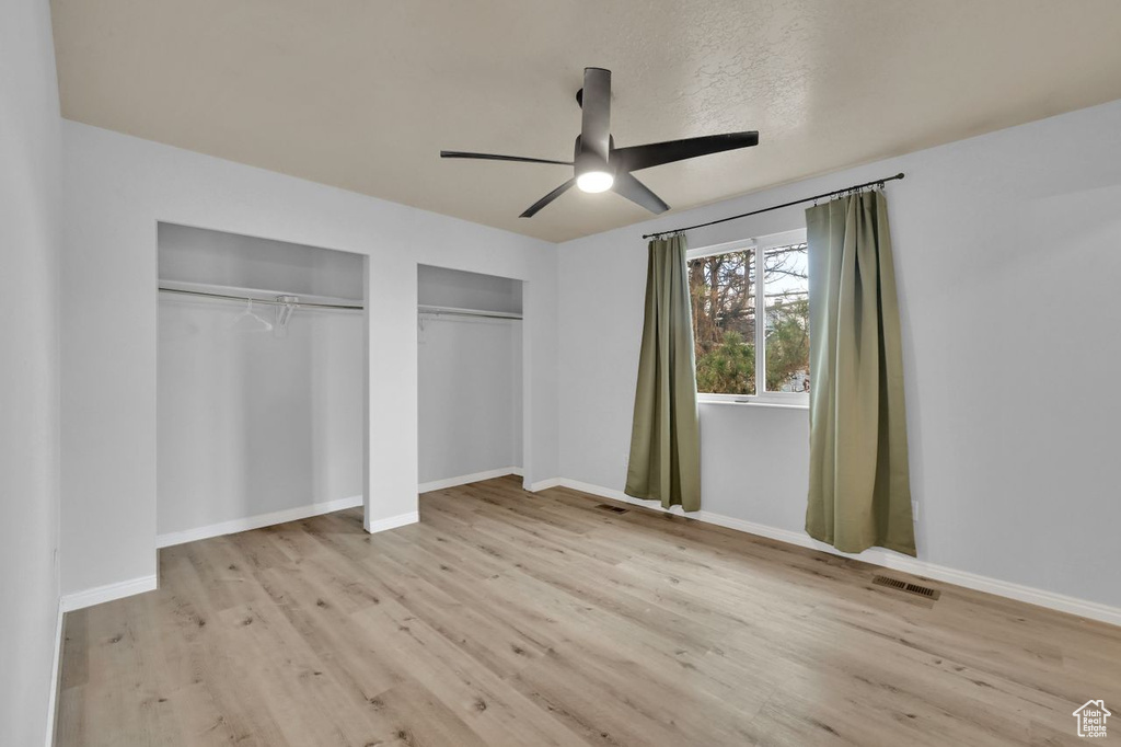 Unfurnished bedroom featuring baseboards, multiple closets, visible vents, and wood finished floors