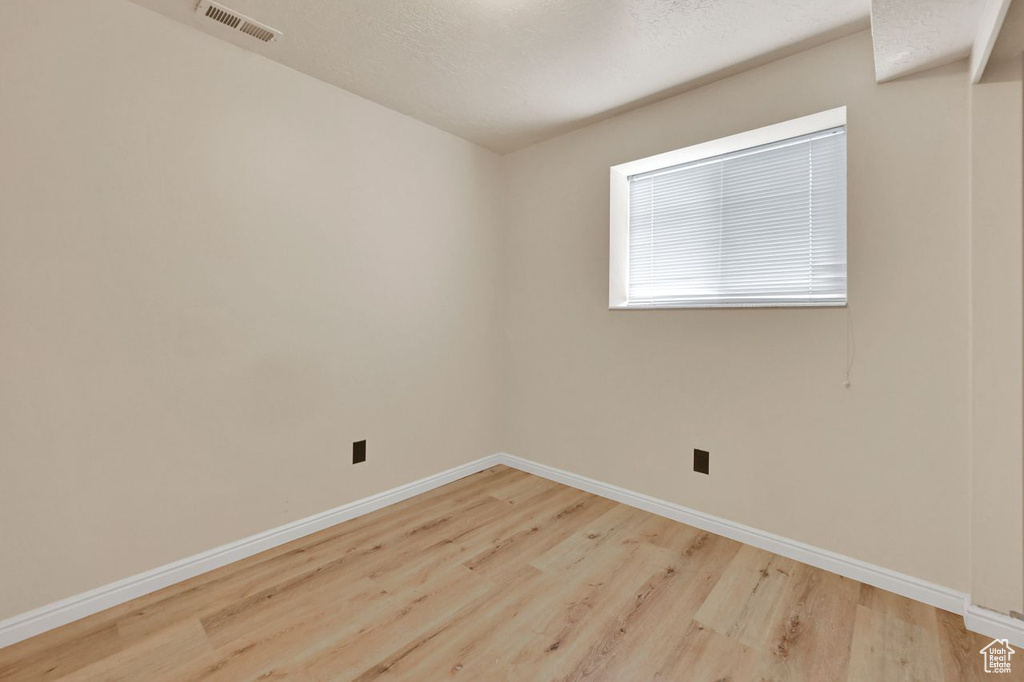 Empty room with wood finished floors, a textured ceiling, baseboards, and visible vents