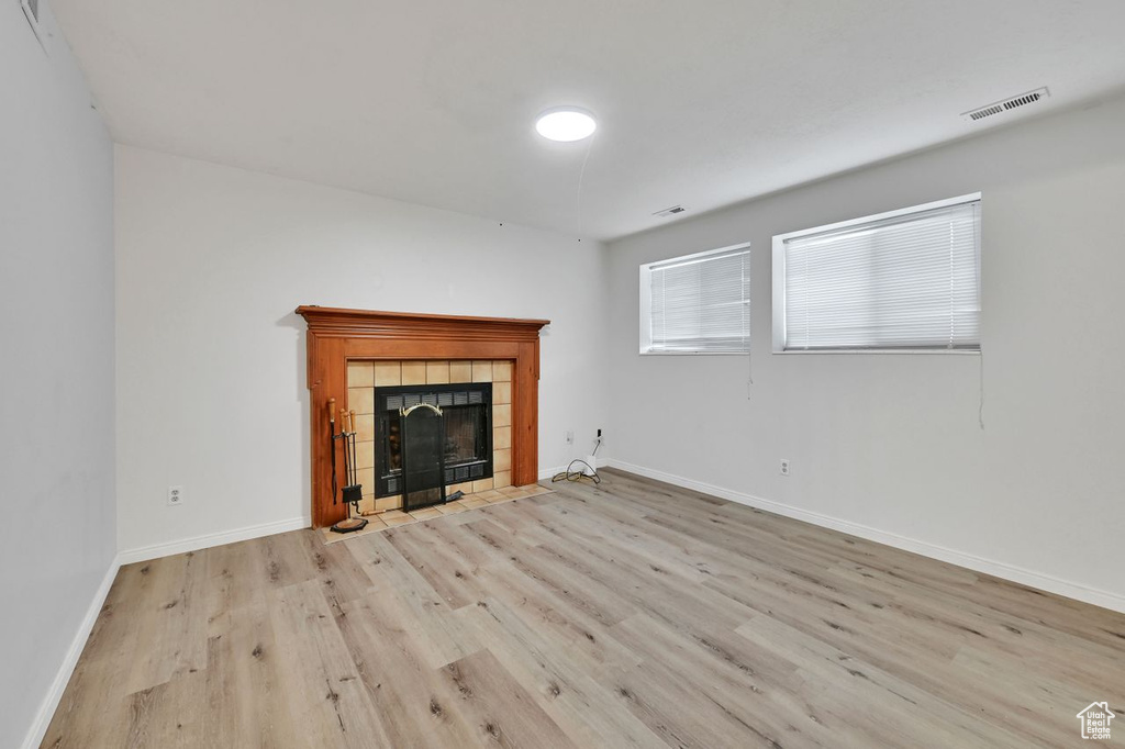Unfurnished living room with visible vents, a tile fireplace, baseboards, and wood finished floors