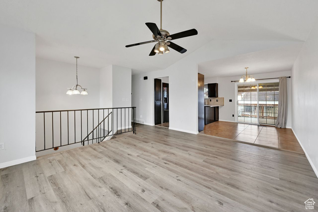 Unfurnished living room featuring ceiling fan with notable chandelier, baseboards, vaulted ceiling, and wood finished floors