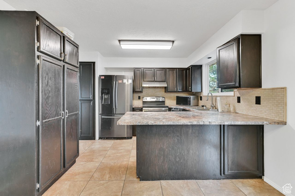 Kitchen with under cabinet range hood, stainless steel electric stove, a sink, a peninsula, and fridge with ice dispenser
