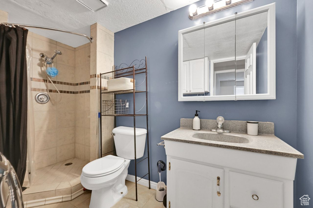 Bathroom with a textured ceiling, baseboards, toilet, a tile shower, and vanity