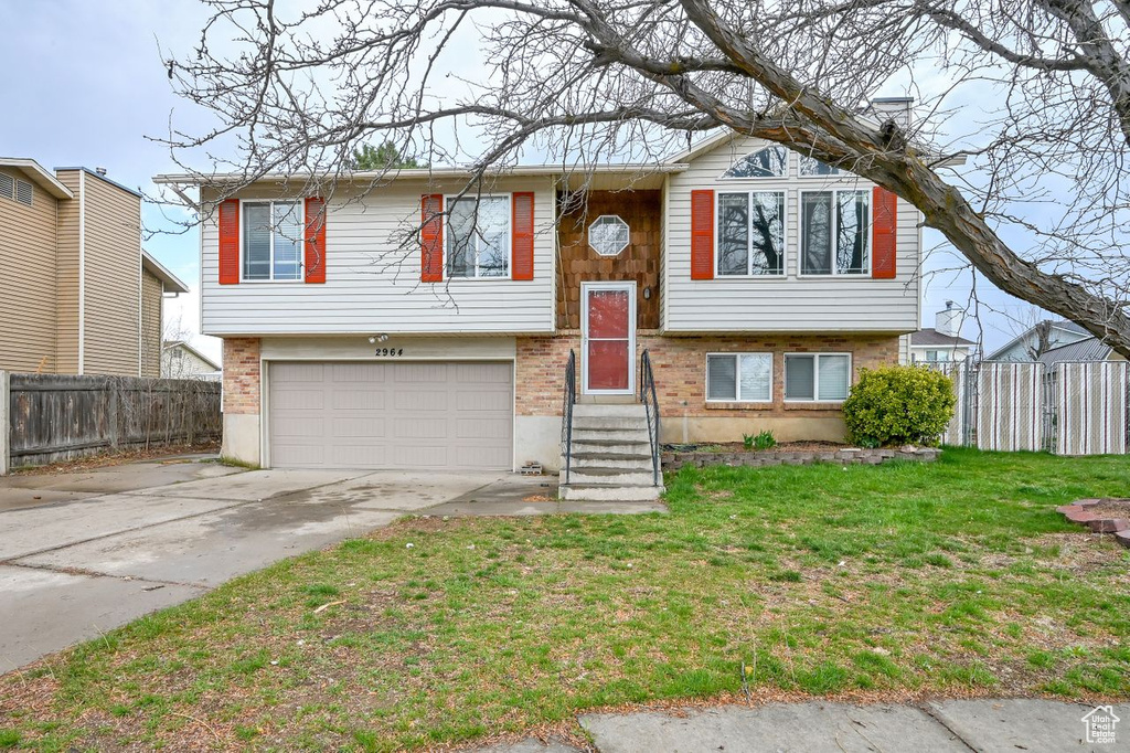 Split foyer home featuring concrete driveway, fence, brick siding, a front lawn, and a garage