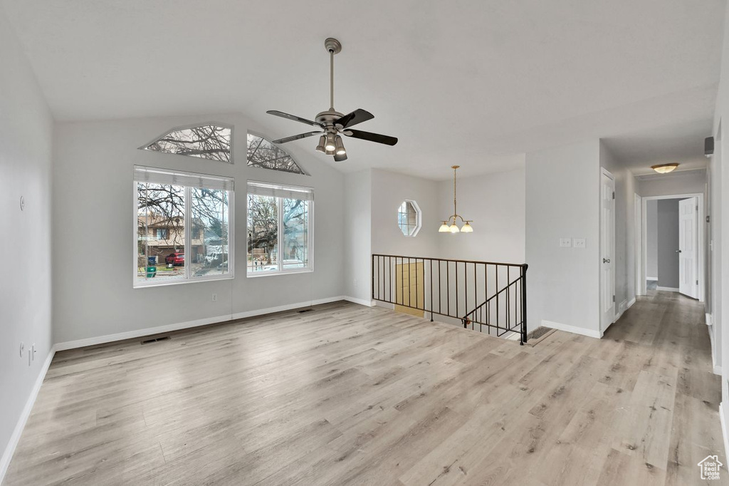 Unfurnished room featuring baseboards, wood finished floors, vaulted ceiling, and ceiling fan with notable chandelier