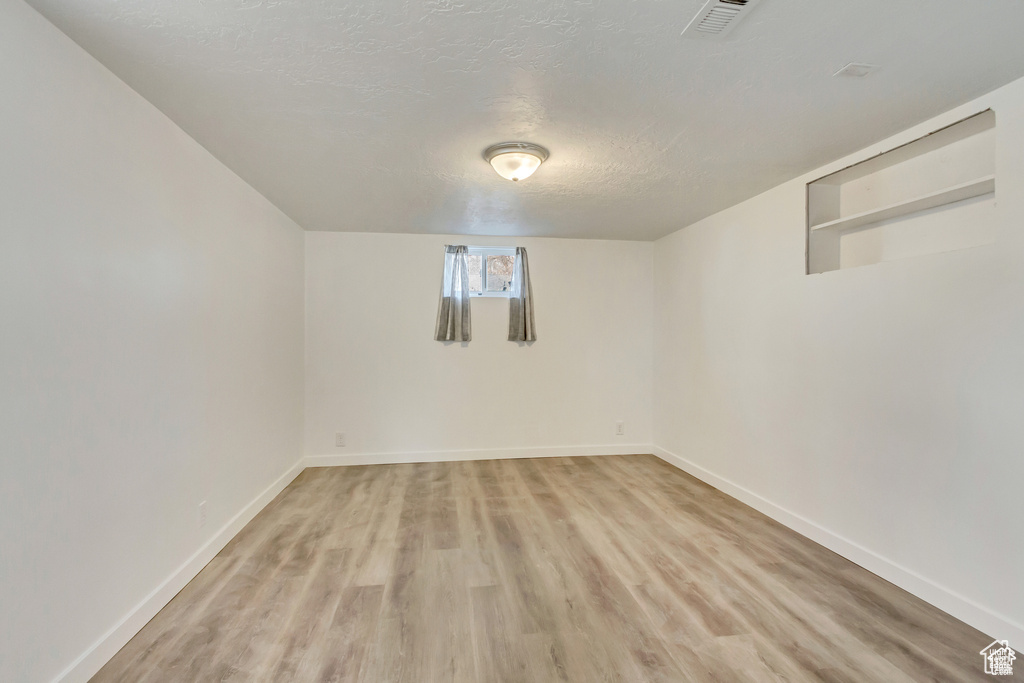Basement with baseboards, a textured ceiling, visible vents, and light wood-type flooring
