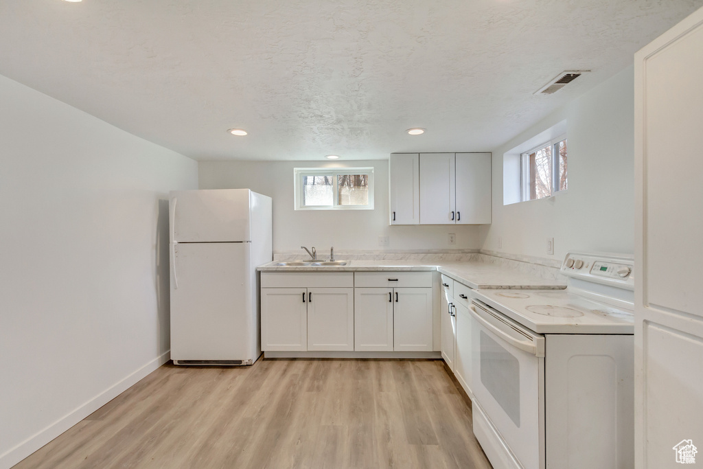 Kitchen with white appliances, baseboards, a sink, light wood-style floors, and visible vents