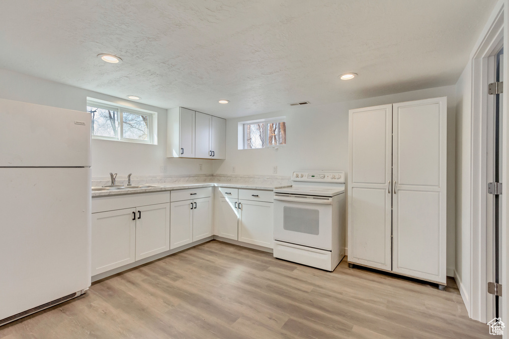Kitchen featuring white cabinets, a sink, light wood-style floors, and white appliances
