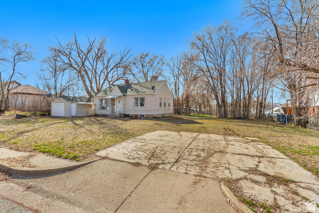View of front of property featuring fence, a chimney, a storage unit, a front lawn, and an outbuilding
