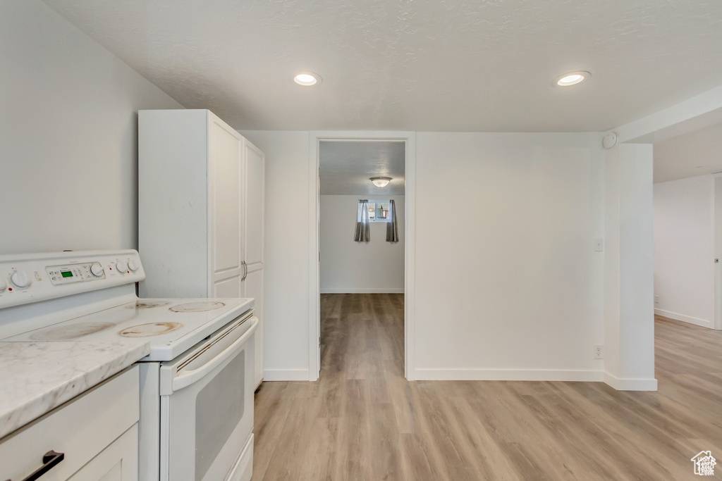 Kitchen with baseboards, white cabinets, electric range, and light wood-style floors