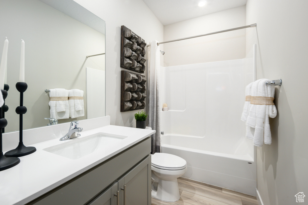Bathroom featuring toilet, wood finished floors, shower / tub combo with curtain, and vanity