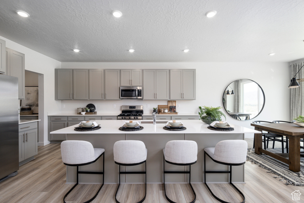 Kitchen with light countertops, stainless steel appliances, gray cabinetry, a breakfast bar, and light wood finished floors