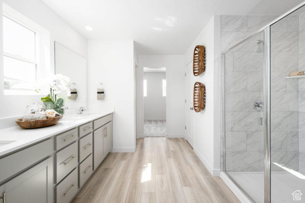 Full bath with baseboards, double vanity, wood finished floors, and a stall shower