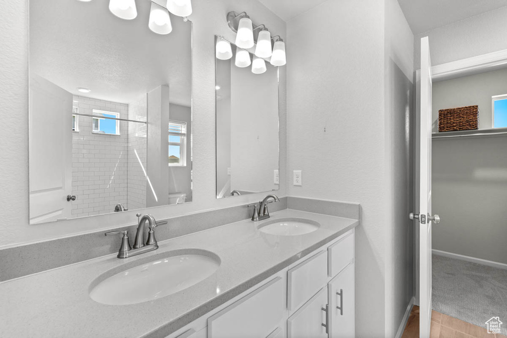 Bathroom featuring a shower, double vanity, a sink, and baseboards
