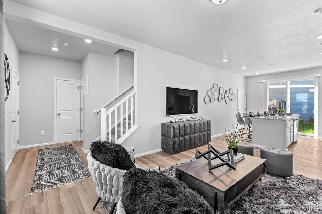 Living room with baseboards, light wood-type flooring, stairs, and recessed lighting