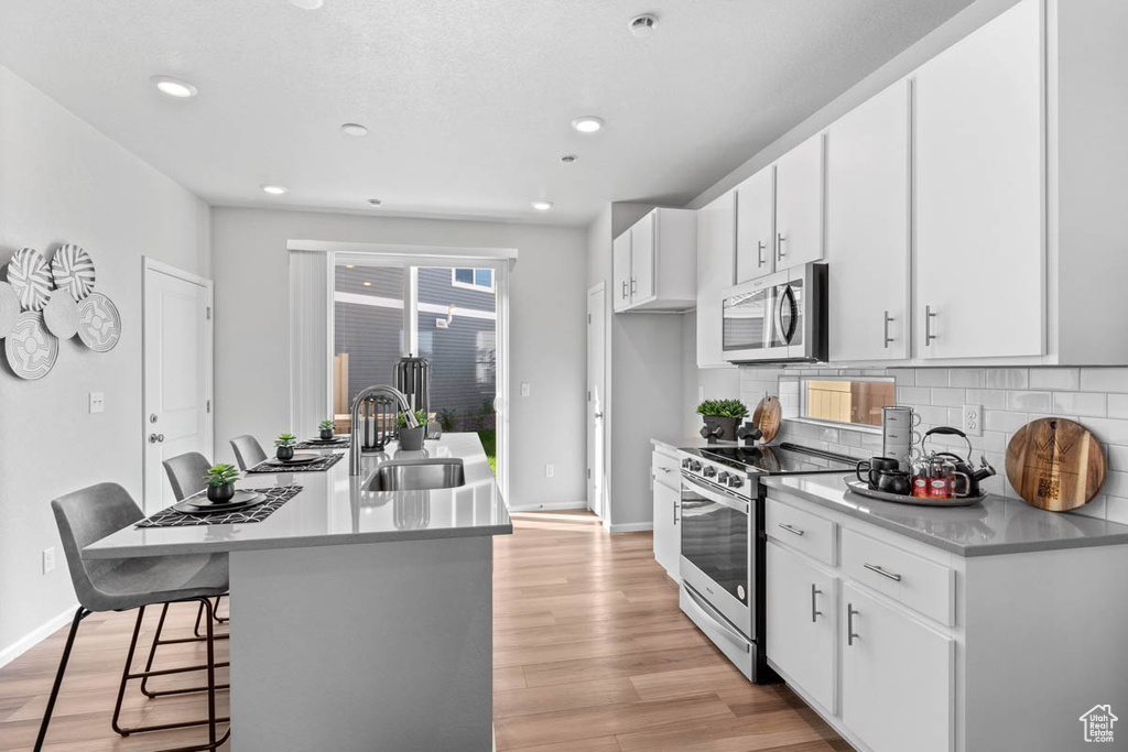 Kitchen with light wood-type flooring, backsplash, a sink, and stainless steel appliances