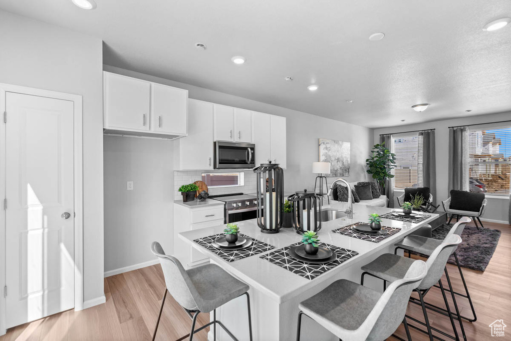 Kitchen with a kitchen breakfast bar, white cabinetry, light wood-type flooring, stainless steel appliances, and a sink