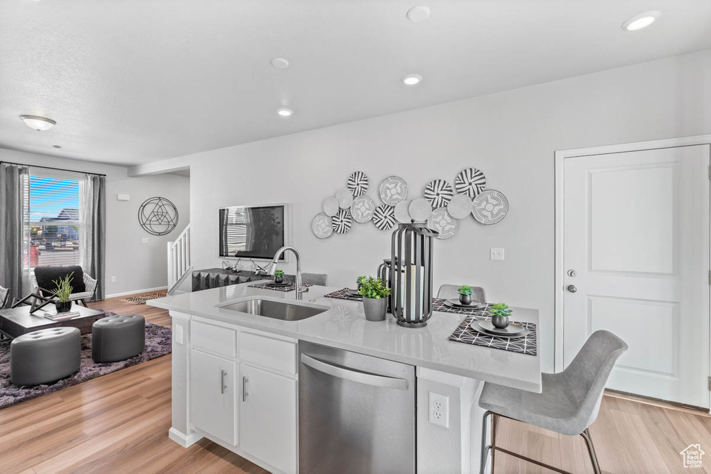 Kitchen featuring open floor plan, a sink, an island with sink, light wood finished floors, and dishwasher