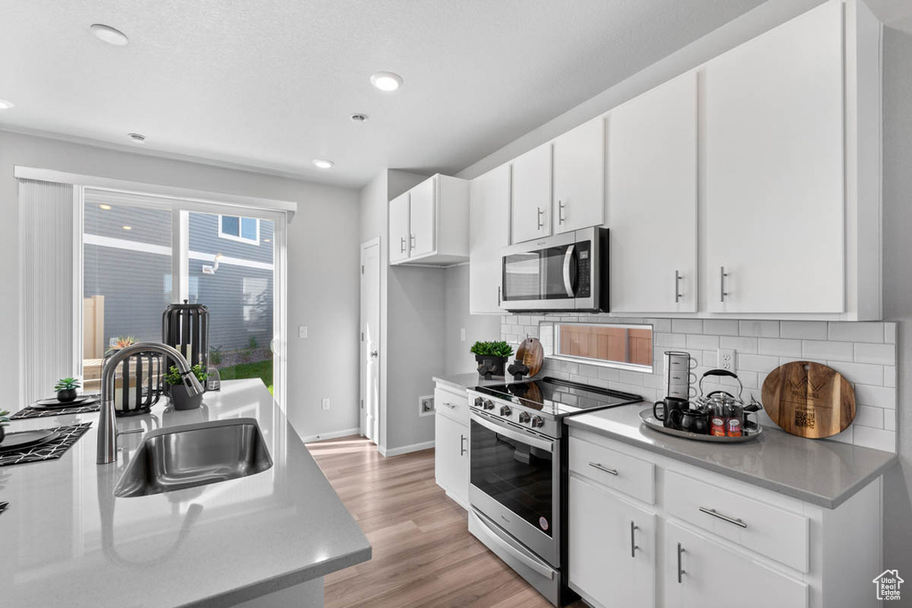 Kitchen featuring a sink, white cabinetry, tasteful backsplash, appliances with stainless steel finishes, and light wood-type flooring