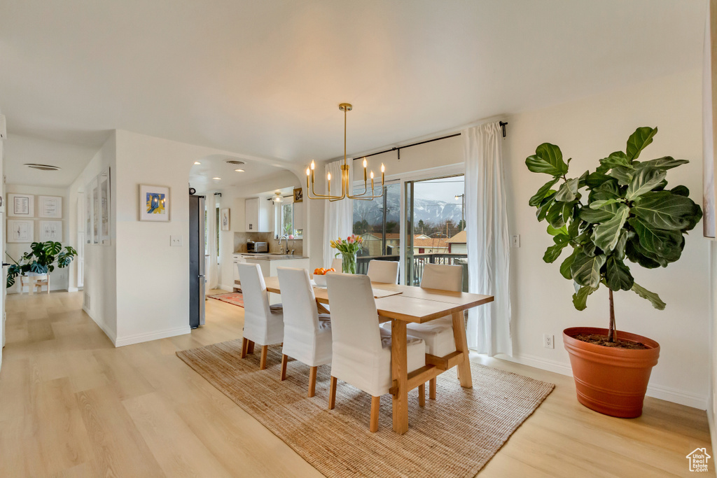 Dining space featuring baseboards, light wood-type flooring, arched walkways, and a chandelier