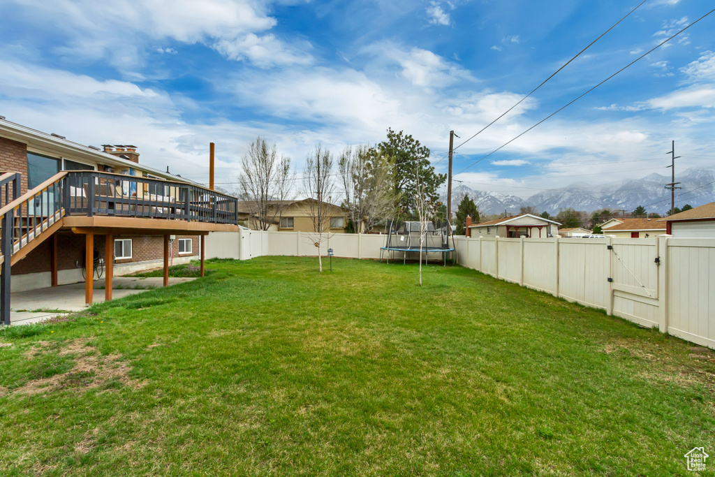 View of yard featuring a trampoline, a fenced backyard, a gate, and a deck with mountain view