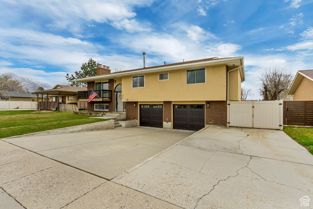 Raised ranch with a gate, an attached garage, a chimney, a front yard, and driveway