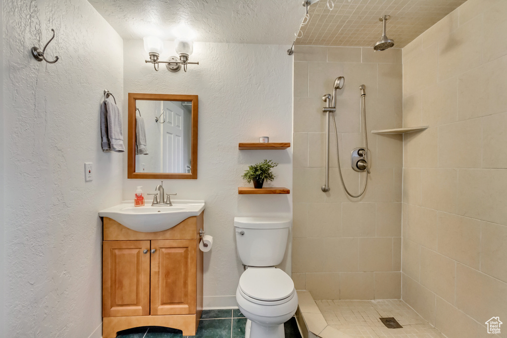 Bathroom featuring vanity, a textured wall, toilet, and tiled shower