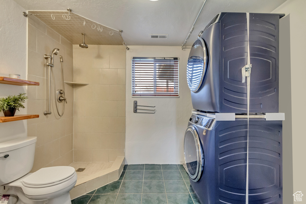 Bathroom featuring visible vents, stacked washer and clothes dryer, a tile shower, toilet, and tile patterned flooring