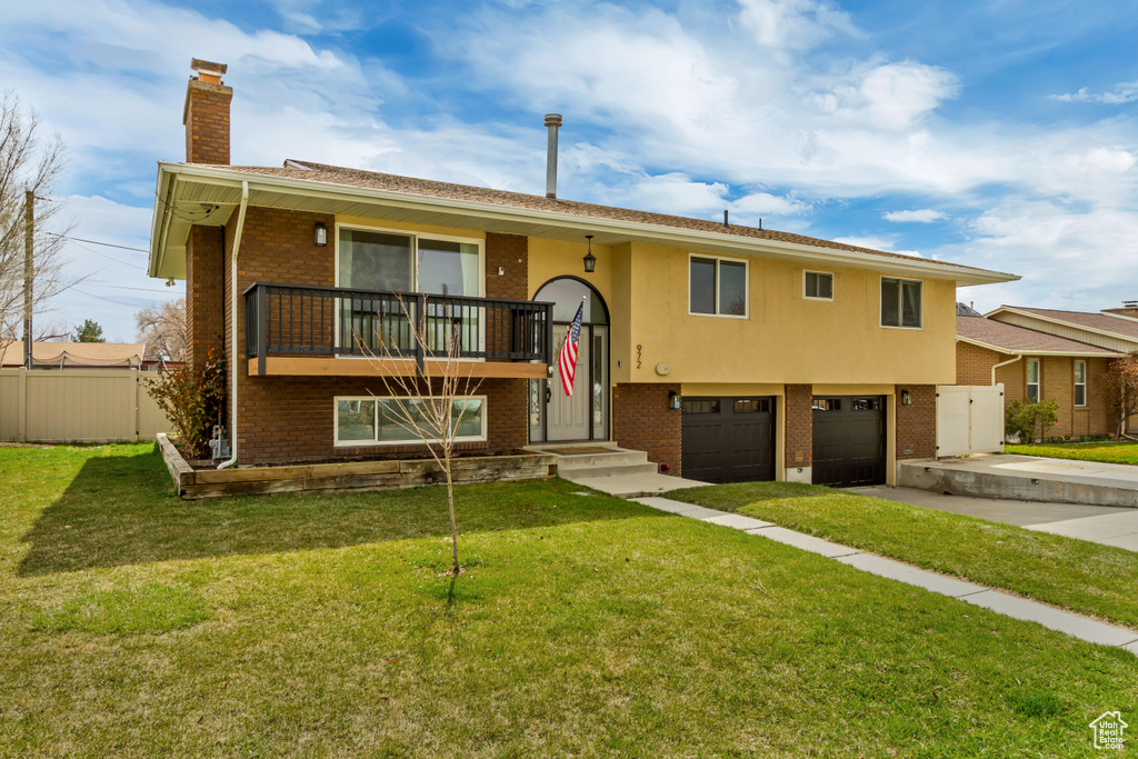 Split foyer home featuring brick siding, concrete driveway, fence, and a front lawn