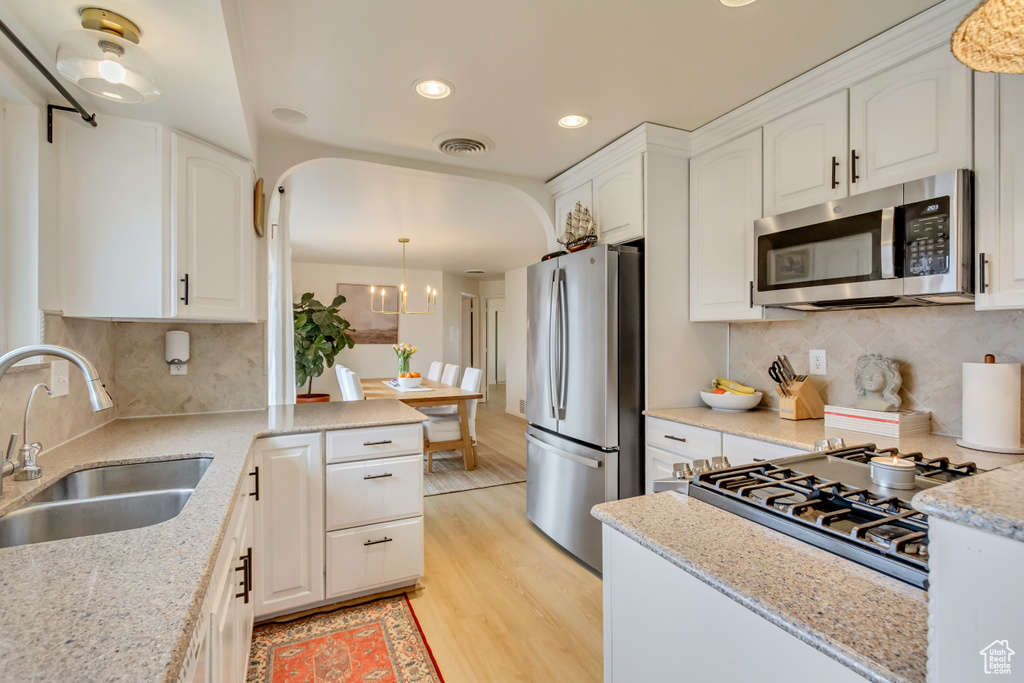 Kitchen with white cabinetry, stainless steel appliances, a sink, visible vents, and light wood-style flooring