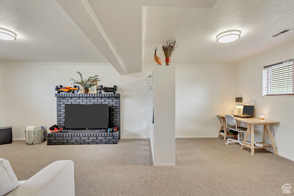 Carpeted office featuring a textured ceiling, visible vents, a brick fireplace, baseboards, and beam ceiling