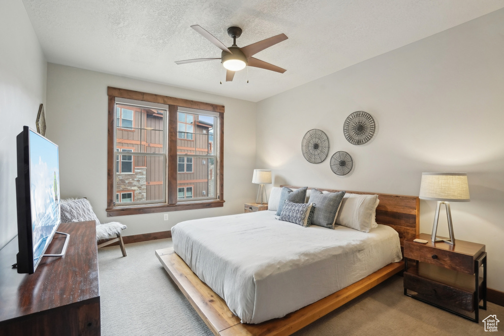 Carpeted bedroom featuring a ceiling fan, baseboards, and a textured ceiling