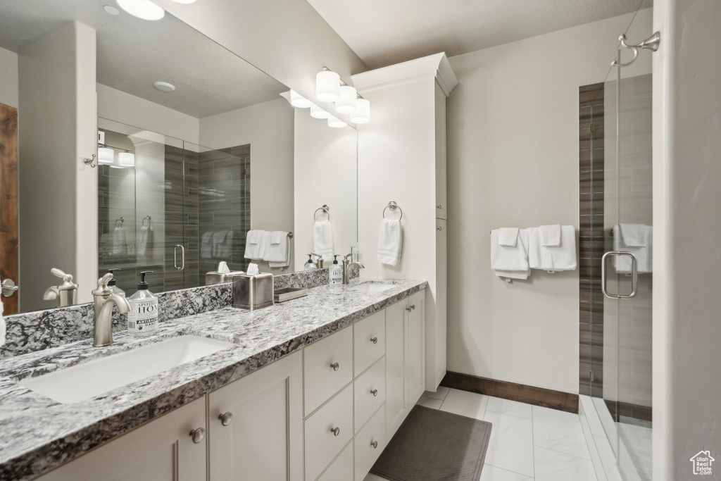 Bathroom featuring a stall shower, double vanity, baseboards, and a sink