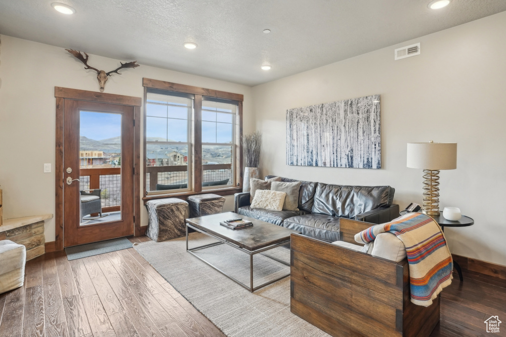 Living room featuring hardwood / wood-style flooring, a textured ceiling, baseboards, visible vents, and recessed lighting